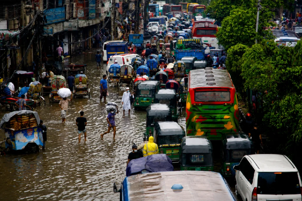 People wading through floodwaters in Dhaka after record rainfall during the Bangladesh Flood 2026, causing widespread flooding, transport disruption, and loss of lives.